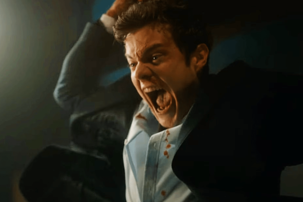 Jack Quaid with his arms over his head and mouth open in a scream